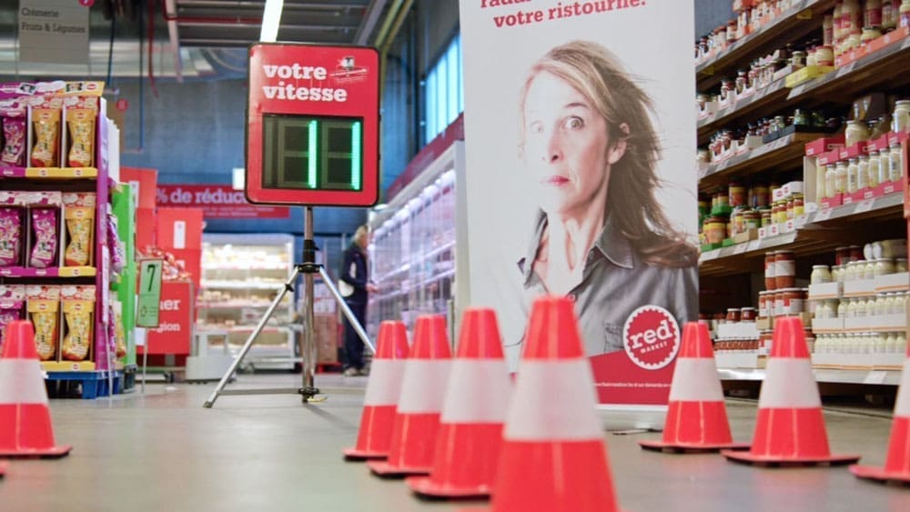 Red Market supermarkt activatie met verkeerskegels, snelheidsradar en campagnebanner in supermarktgang